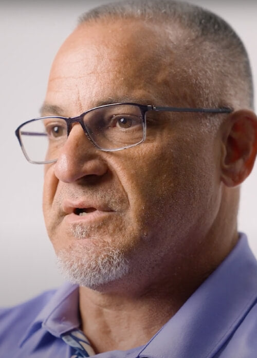 A headshot of a man in glasses wearing a purple shirt