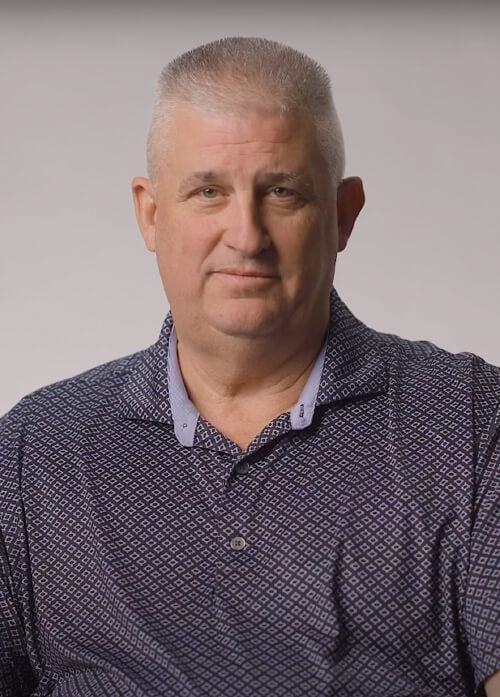 A headshot of a man in a patterned collared shirt